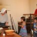Becky, a cook at Gunston Hall, demonstrates to visitors Laura, Paul and their father, Oliver, how to cook a fish by strapping it to a board and placing it near the fire. (Mary Davidson/PotomacLocal.com)